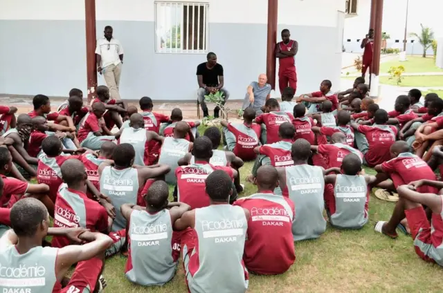 Young players aged 12-14 sit on the ground listening to coaches during a training session at Génération Foot.